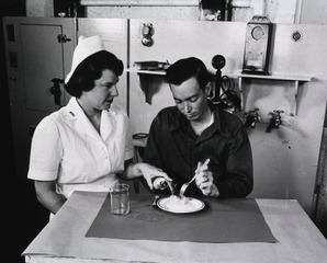 [A female therapist instructs a male amputee in the use of his prothesis]