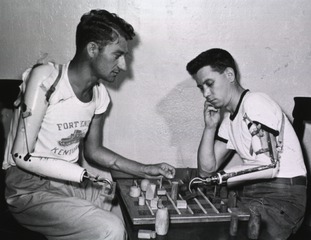 [Two men with prosthetic arms playing a game of checkers as part of rehabilitation]