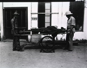 [Transportation of wounded on a wheeled stretcher in front of an X-ray building]