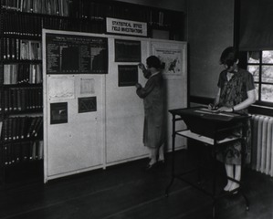[Two women posting charts on a bulletin board]