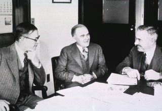 [Thomas Parran and two men seated at a desk]
