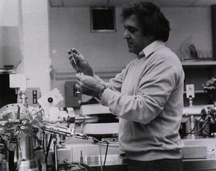 [Unidentified man in a laboratory inserting a syringe in a bottle]