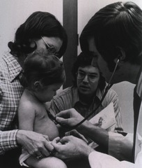 A National Health Service Corps physician listens to the heartbeat of an infant