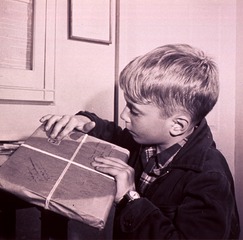 [Boy (head-and-shoulders portrait, facing left) placing a postage stamp on an airmail package]