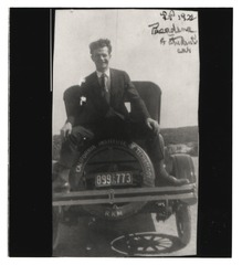 Linus Pauling sitting on the back of a car with his legs spread out over the wheel
