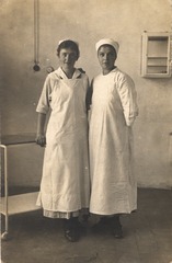 [Two women in white caps and aprons standing together]